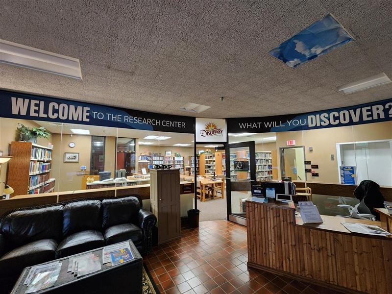 photo of the Iron Range Research Center with a new wrap banner around the glass interior entrance. The wrap reads: Welcome to the Research Center, what will you discover? With the Minnesota Discovery Center logo.